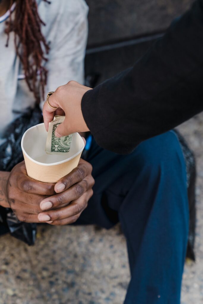 A person giving money to a homeless man seated outdoors in a gesture of compassion.